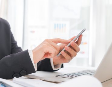 Closeup of business woman hand typing on laptop keyboard with  mobile phone